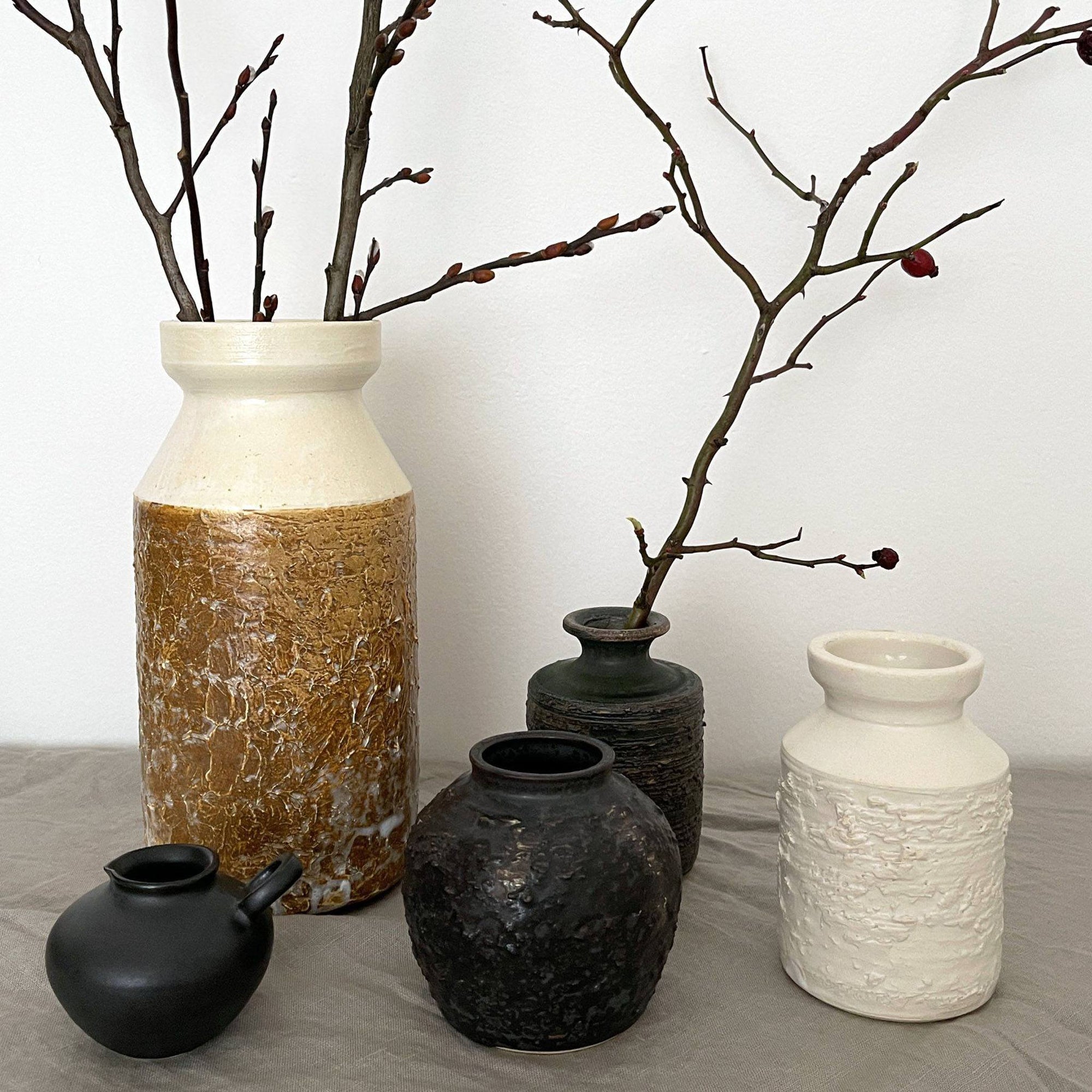 Assorted ceramic vases with textured surfaces and branches, showcasing modern rustic decor style.