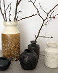 Assorted ceramic vases with textured surfaces and branches, showcasing modern rustic decor style.