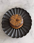 Elegant black Rinka Plate by Yoshida Pottery holding a chocolate donut with sprinkles on a marble surface.