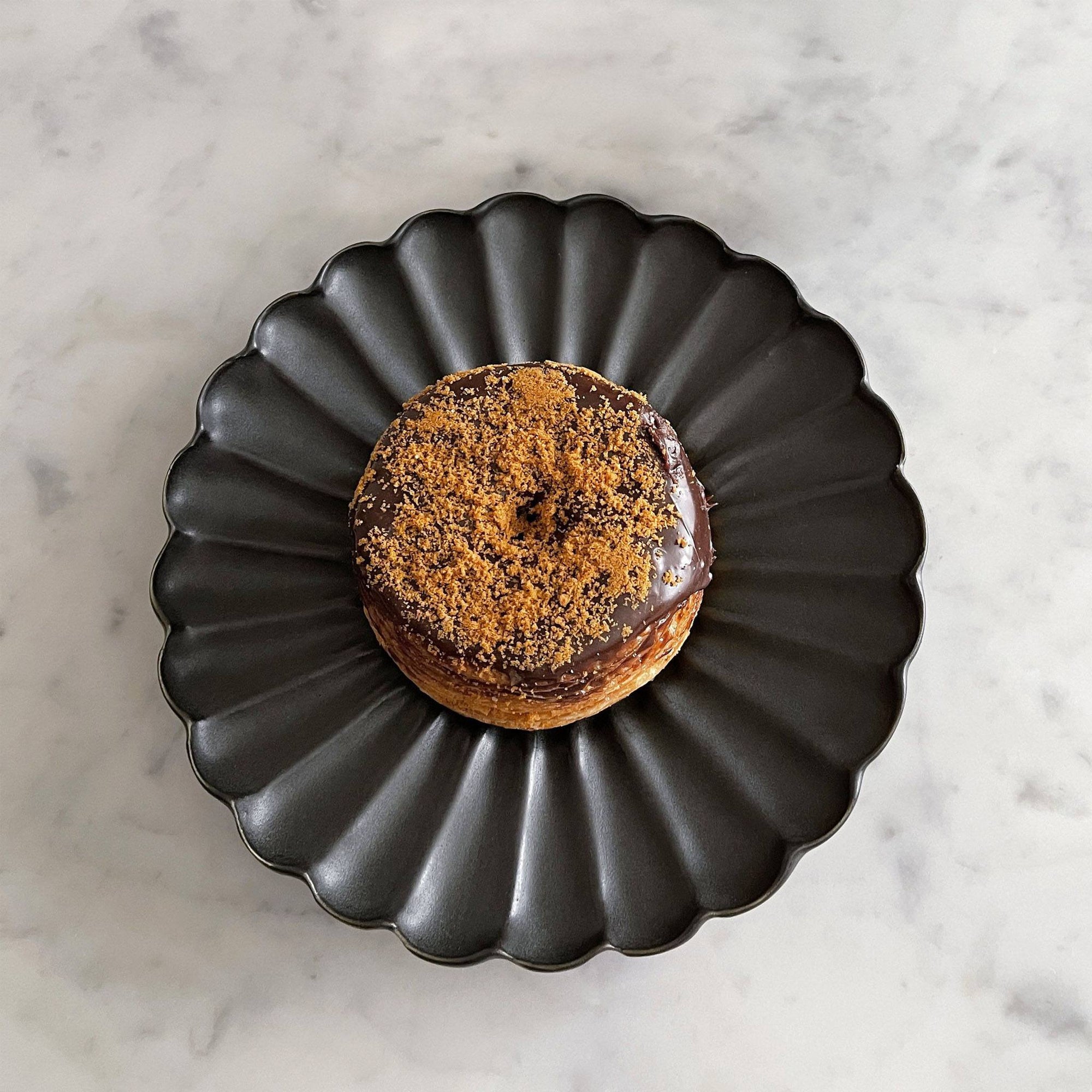 Elegant black Rinka Plate by Yoshida Pottery holding a chocolate donut with sprinkles on a marble surface.