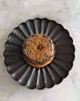 Elegant black Rinka Plate by Yoshida Pottery holding a chocolate donut with sprinkles on a marble surface.