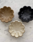 Three Rinka Bowls in flower shape, handcrafted porcelain with beige, black, and cream colors on a marble surface.