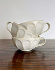 Stack of white porcelain Rinka soup cups with flower design by Kaneko Kohyo on a wooden table.