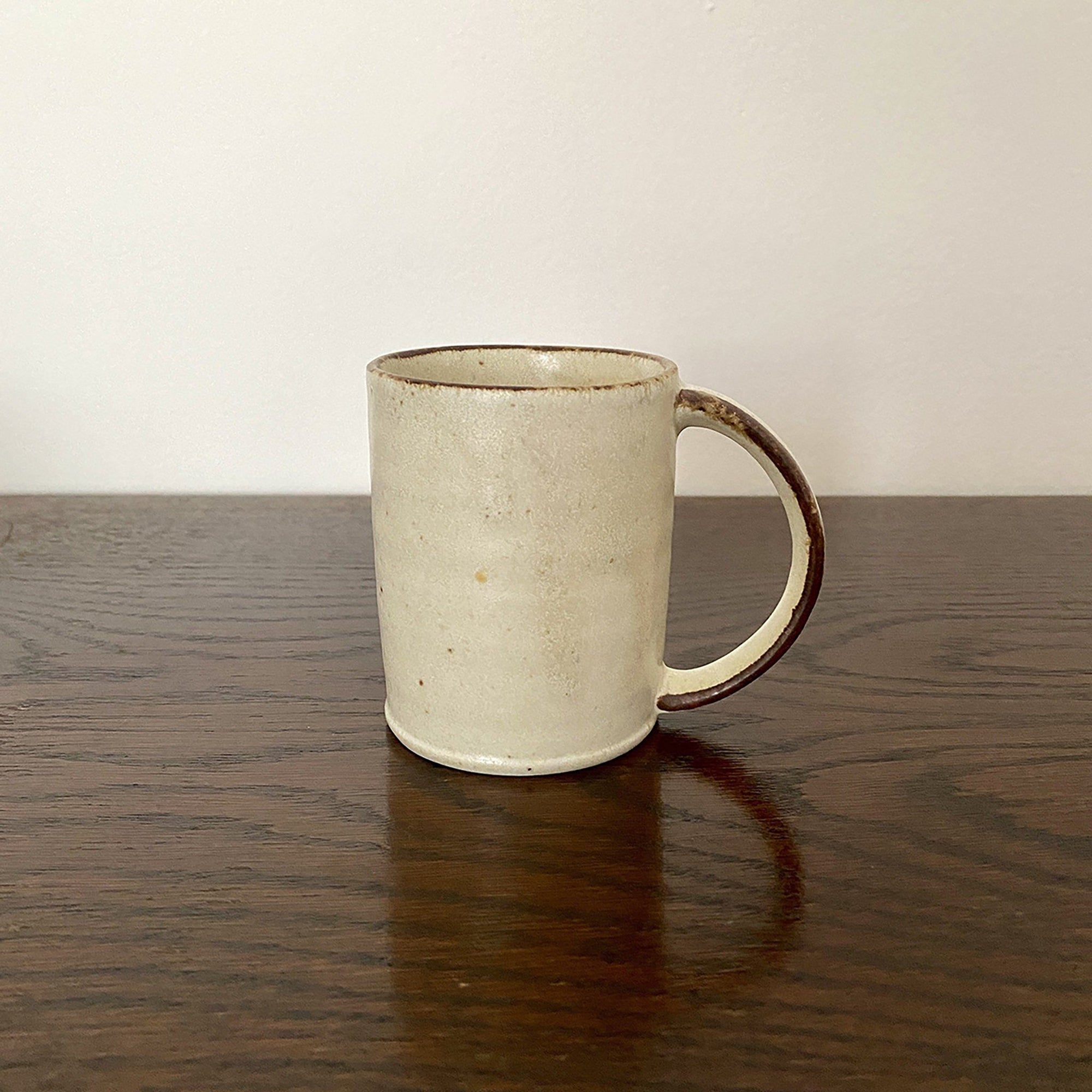 Rila Ivory Straight Mug, textured porcelain, microwave-safe, stackable, warm matte finish, compact size, on dark wood surface.