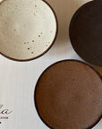 Three Rila 16cm porcelain plates with matte texture by Kaneko Kohyo, showcasing warm colors, perfect for relaxation. Made in Japan.