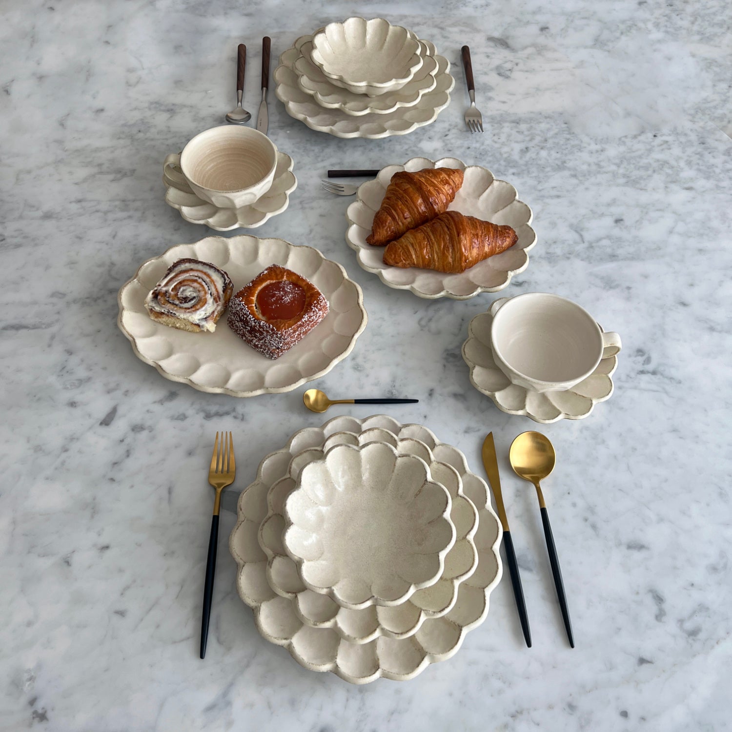 Elegant dining set with scalloped plates and bowls for two, featuring pastries, showcasing Japanese and Western design blend.