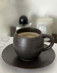 Rila Black Mug from Kaneko Kohyo, textured porcelain, on a table, filled with coffee, microwave-safe, matte finish, 340ml capacity.