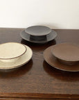 Japanese porcelain plates by Kaneko Kohyo, including Rila Brown, featuring tasteful textures and matte finish, displayed on a wooden table.