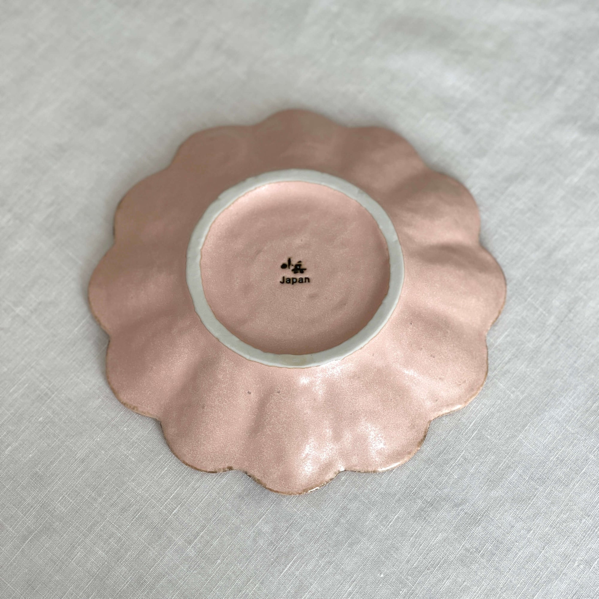 Rinka Plate 17cm in pink porcelain, handcrafted in Japan, showcasing scalloped edge design on a textured surface.