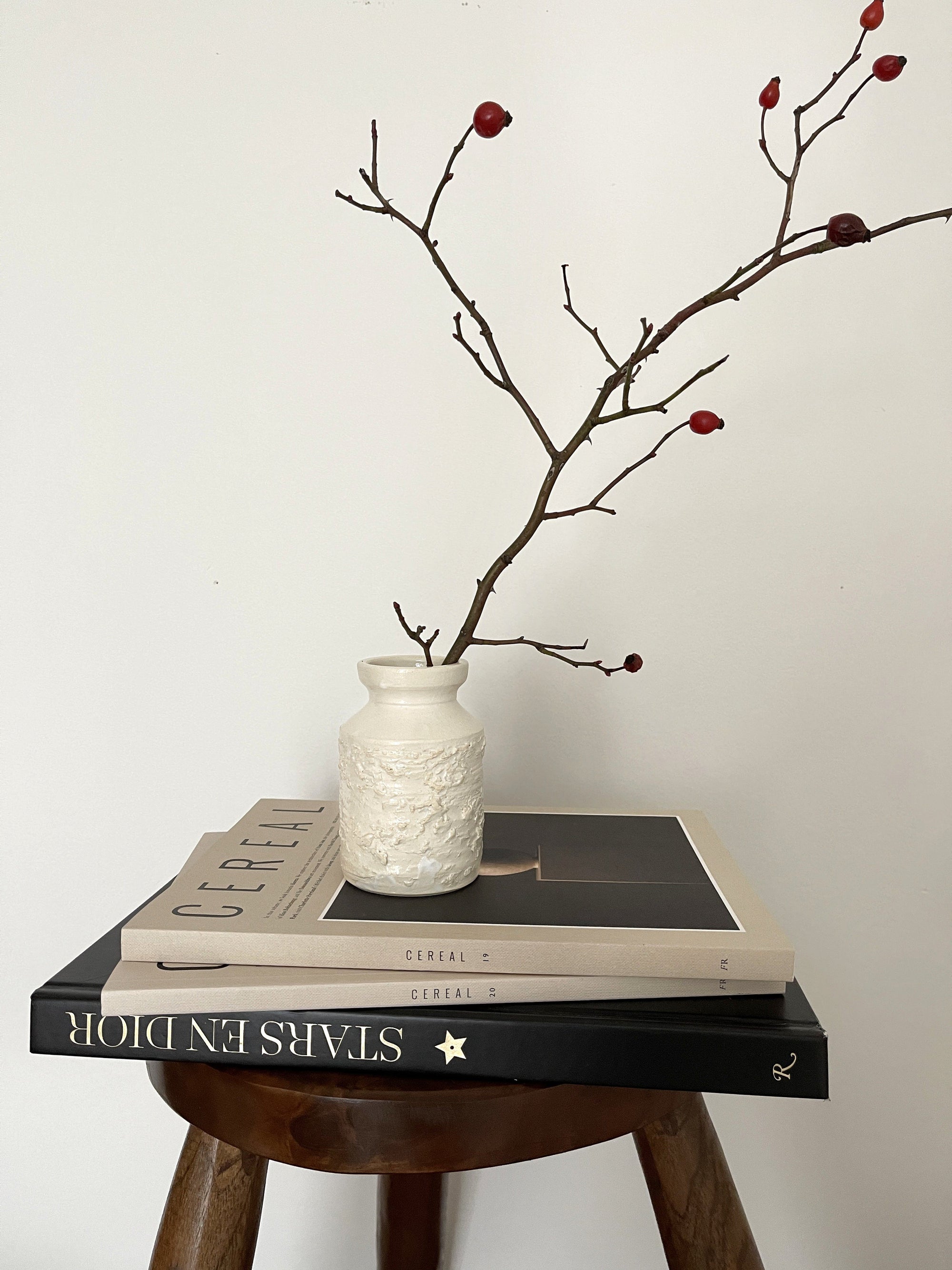 White vase with branches on stacked books, minimalist decor on wooden stool.