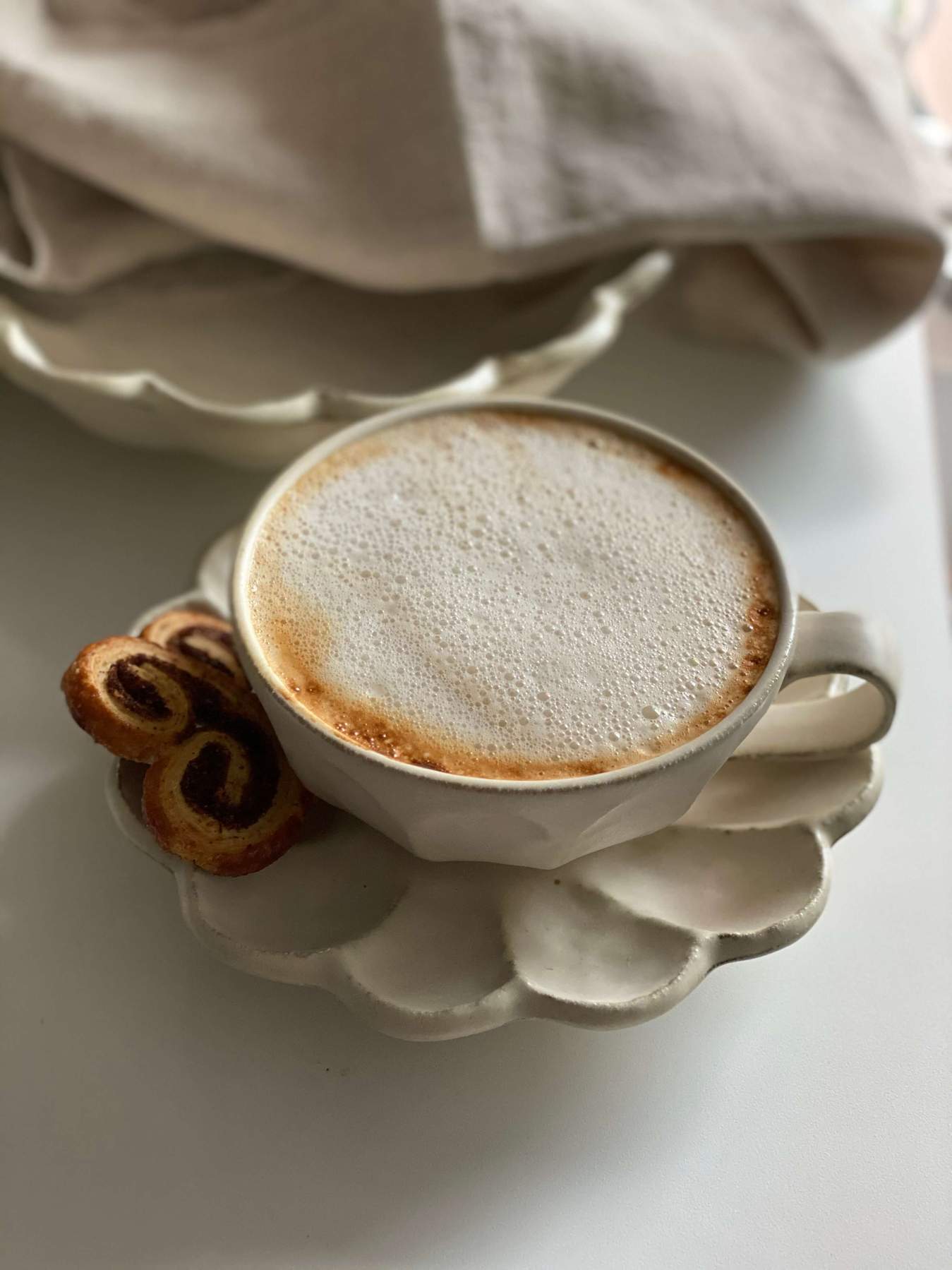 Rinka porcelain cup with frothy coffee on flower-shaped plate by Kaneko Kohyo, showcasing elegant white design and delicate craftsmanship.