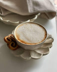 Rinka porcelain cup with frothy coffee on flower-shaped plate by Kaneko Kohyo, showcasing elegant white design and delicate craftsmanship.