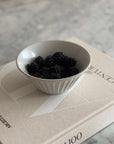White porcelain bowl filled with blackberries set on a book on a marble surface.