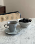 Elegant porcelain cup and bowl on marble table, filled with tea and blackberries.