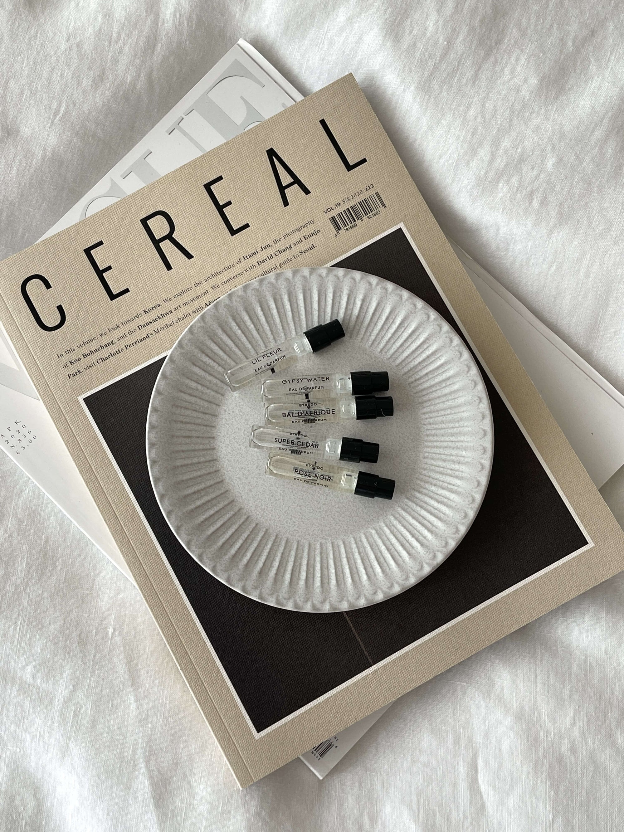 White porcelain plate with ribbed edges on magazine, featuring small vials, evokes nostalgia and elegance.
