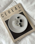 White porcelain plate with ribbed edges on magazine, featuring small vials, evokes nostalgia and elegance.