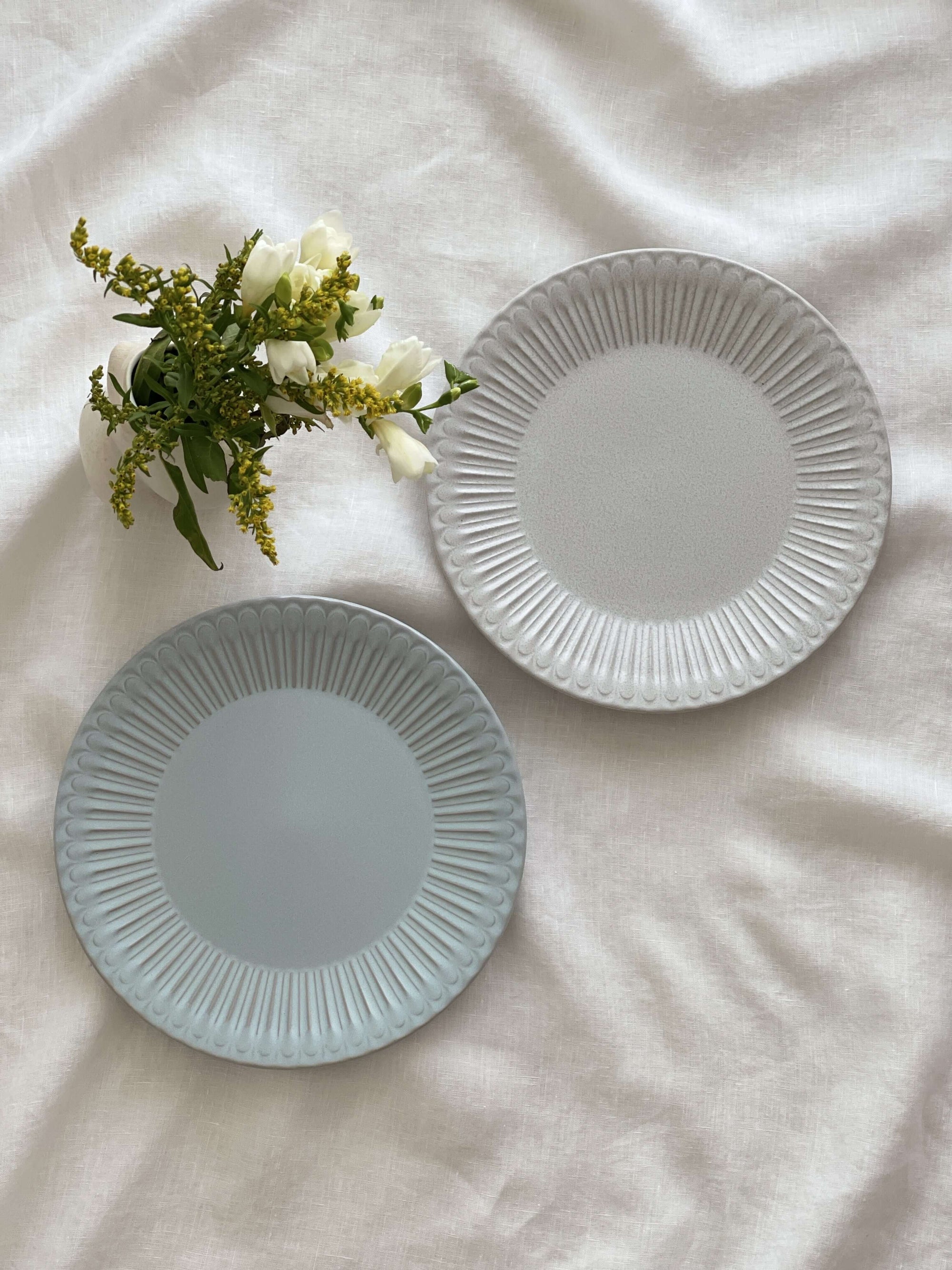 Elegant porcelain plates with lace edges and flowers display on white cloth.