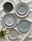 Elegant vintage-style porcelain plates with lace edges and flecked finish, arranged on a white cloth, alongside white flowers.