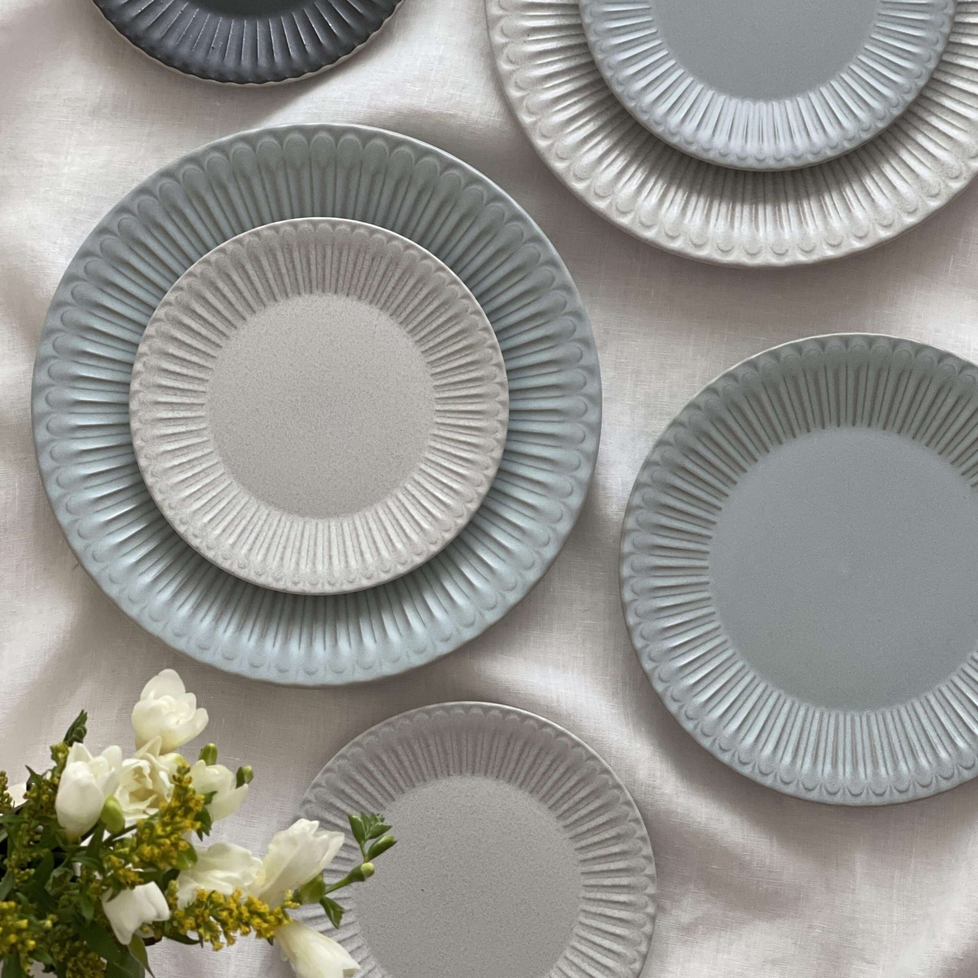 Elegant Storia Plates with lace edges and flecked finish on a table, evoking nostalgia and romance, made of porcelain.