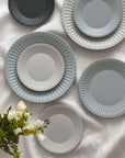 Elegant porcelain plates with soft lace edges and flecked lacquer finish, displayed on a white cloth with flowers.