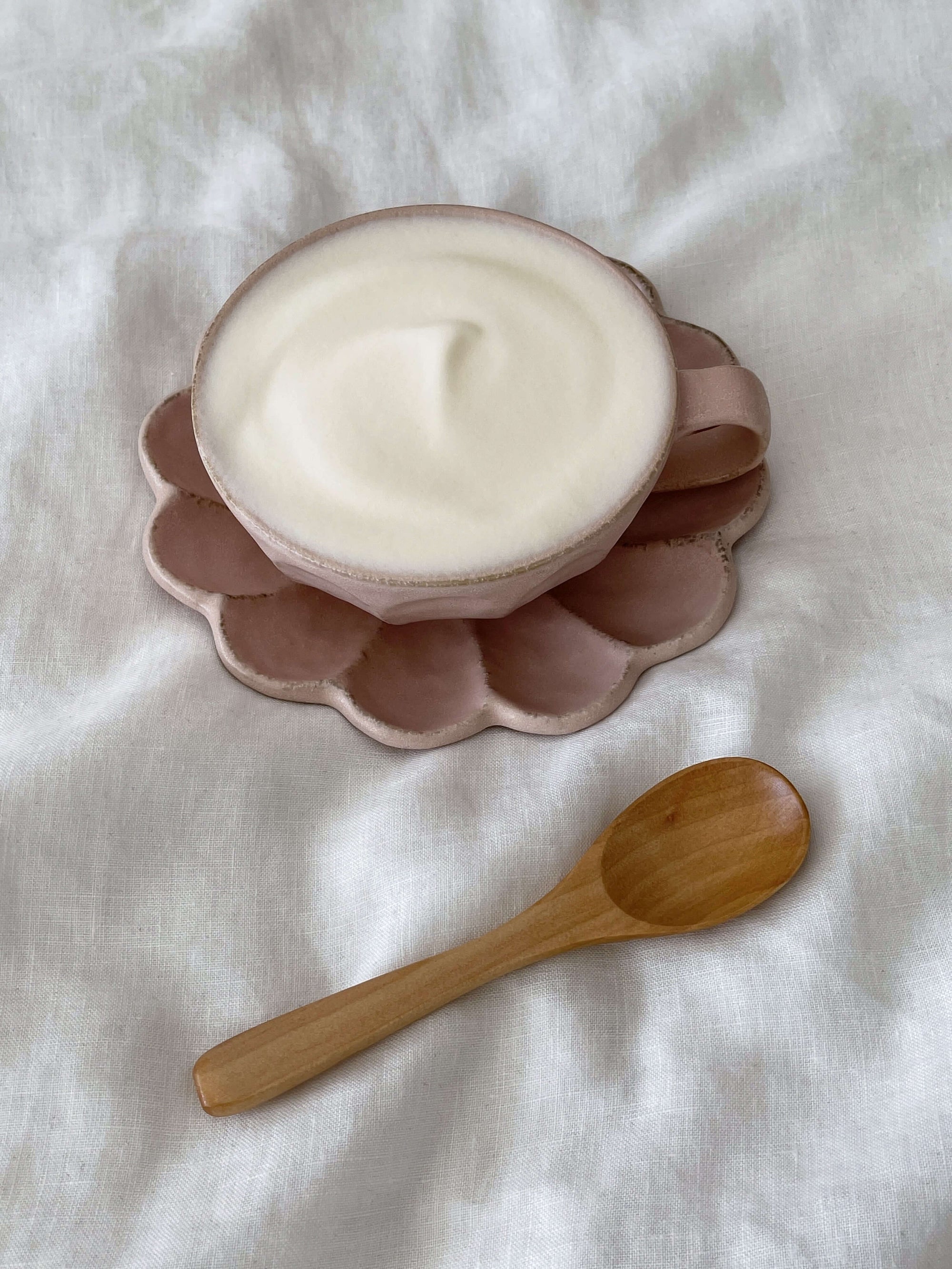 Wooden spoon next to a cup of foamy beverage on a pink saucer.