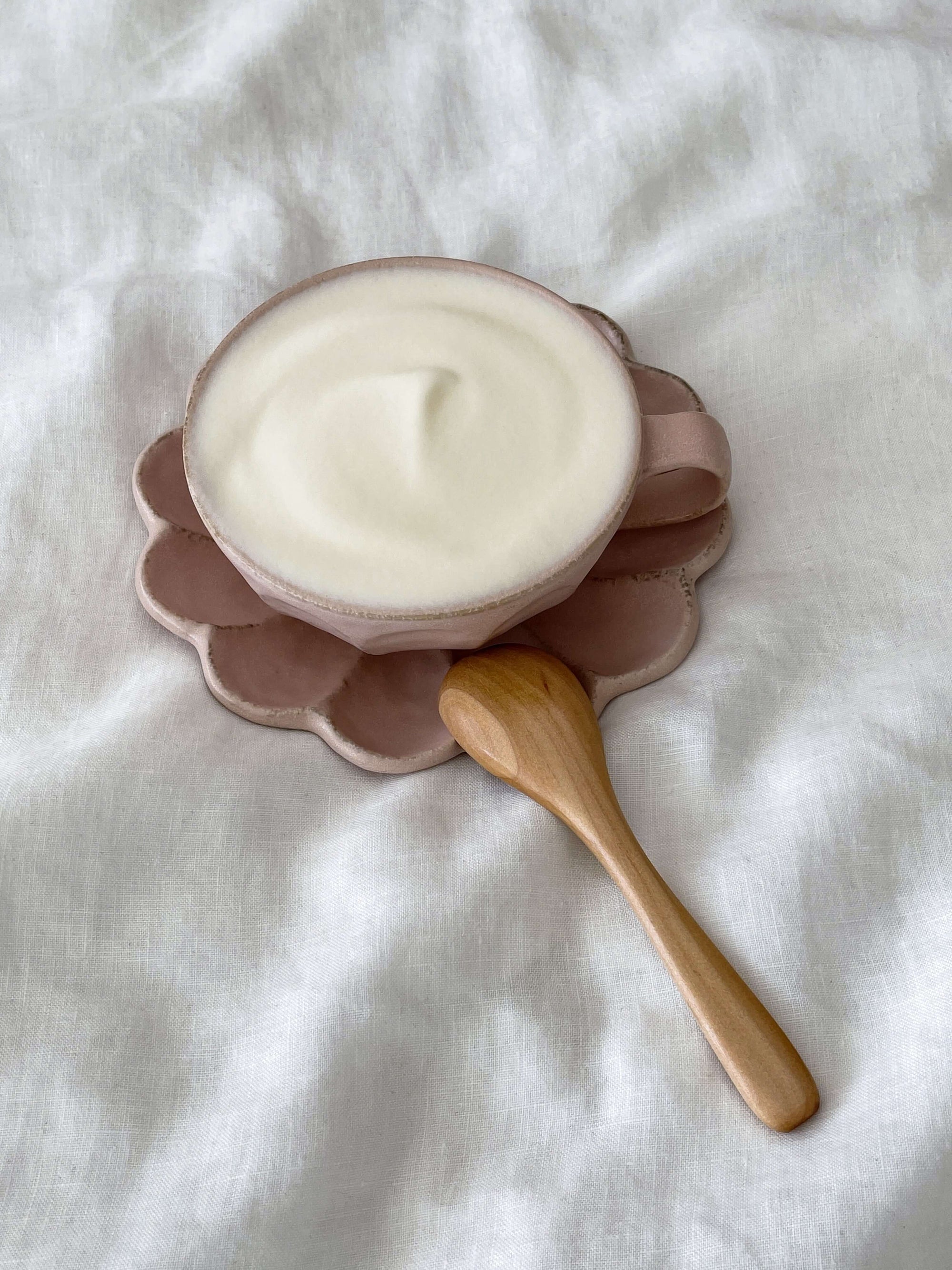 Small wooden spoon next to a bowl of creamy yogurt on a petal-shaped plate.