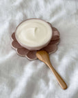 Small wooden spoon next to a bowl of creamy yogurt on a petal-shaped plate.