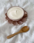 Wooden spoon next to a cup of foamy beverage on a pink saucer.