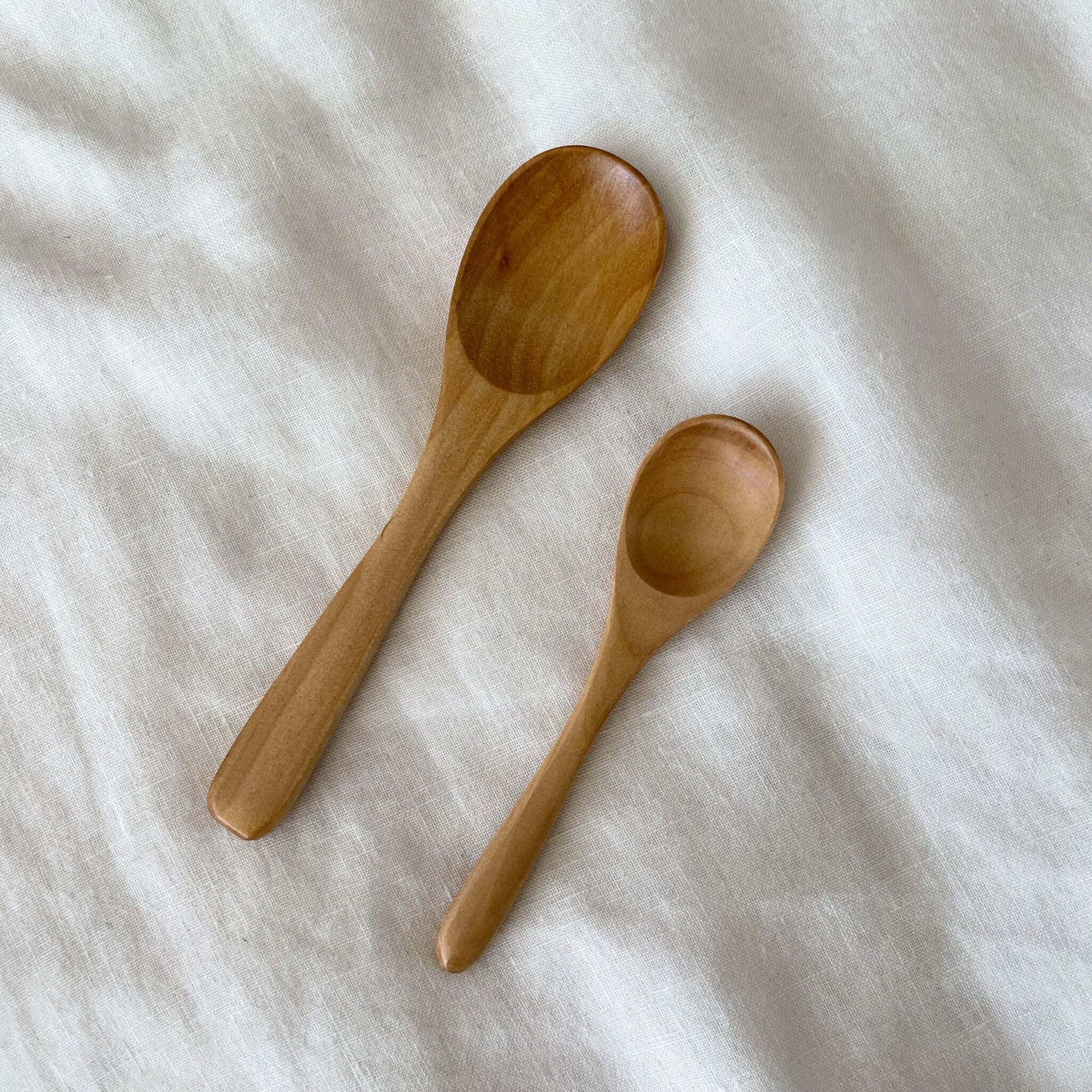 Wooden teaspoons on fabric, featuring a 12.1cm natural wood design ideal for tea or coffee, safe for dishwasher use.