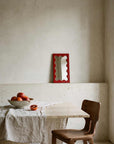 Poppy Red Onda Wave Mirror on a dining table with fruit
