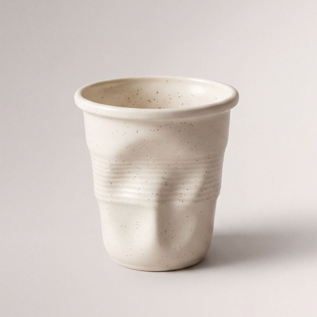 Tazza beige che mette in mostra la sua finitura ceramica opaca e punteggiata.