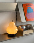 Lumi Poire Lamp, pear-shaped frosted glass lamp lit on a shelf with books