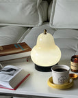 Lumi Poire Lamp lit beside an open book and a coffee cup