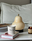 Lumi Poire Lamp lit on a sofa side table with a coffee cup and candle