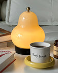 Lumi Poire Lamp lit on a yellow tray with a coffee cup