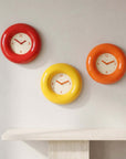 Bagel Clocks in red, yellow and orange arranged on a wall