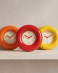 Bagel Clocks in orange, red and yellow lined up on a shelf