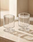 Two clear Sculpted Pedestal Glasses on a travertine surface