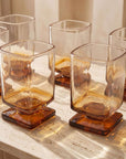 Sculpted Pedestal Glasses in brown with drinks, casting amber shadows