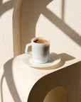 Classic White Pastel Muse Mug with espresso on a stone table