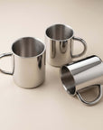 Three Double-Wall Glossy Stainless Steel Cups with round handles, one lying on its side