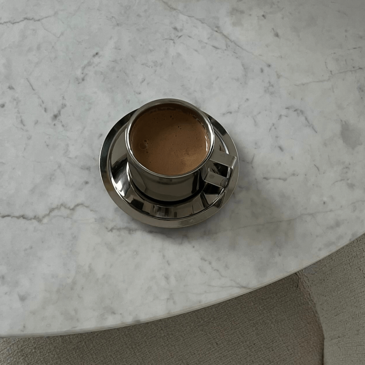 Italian style steel latte coffee cup with saucer on marble table, featuring double-layered design for thermal insulation.