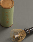 Smoked bamboo Artisan Matcha Whisk lying beside its storage tube