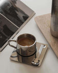 Venice Mirror Cup with coffee on its square saucer beside a magazine