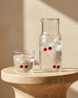 Cherry Glass Pitcher and cup with iced water on a stone side table