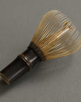 Artisan Bamboo Matcha Whisk in smoked bamboo, resting on its side