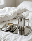 Morning Coffee Set with Monaco cup and French press on an oval steel tray on a bed