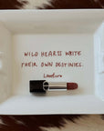 Wild Hearts ceramic tray with a lipstick on a cowhide rug, showing the inscription