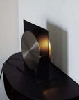 Bauhaus Aura Bedside Lamp seen from the side with its round brushed disc lit