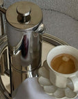 Rinka mug with coffee on its petal plate beside the mirror French press